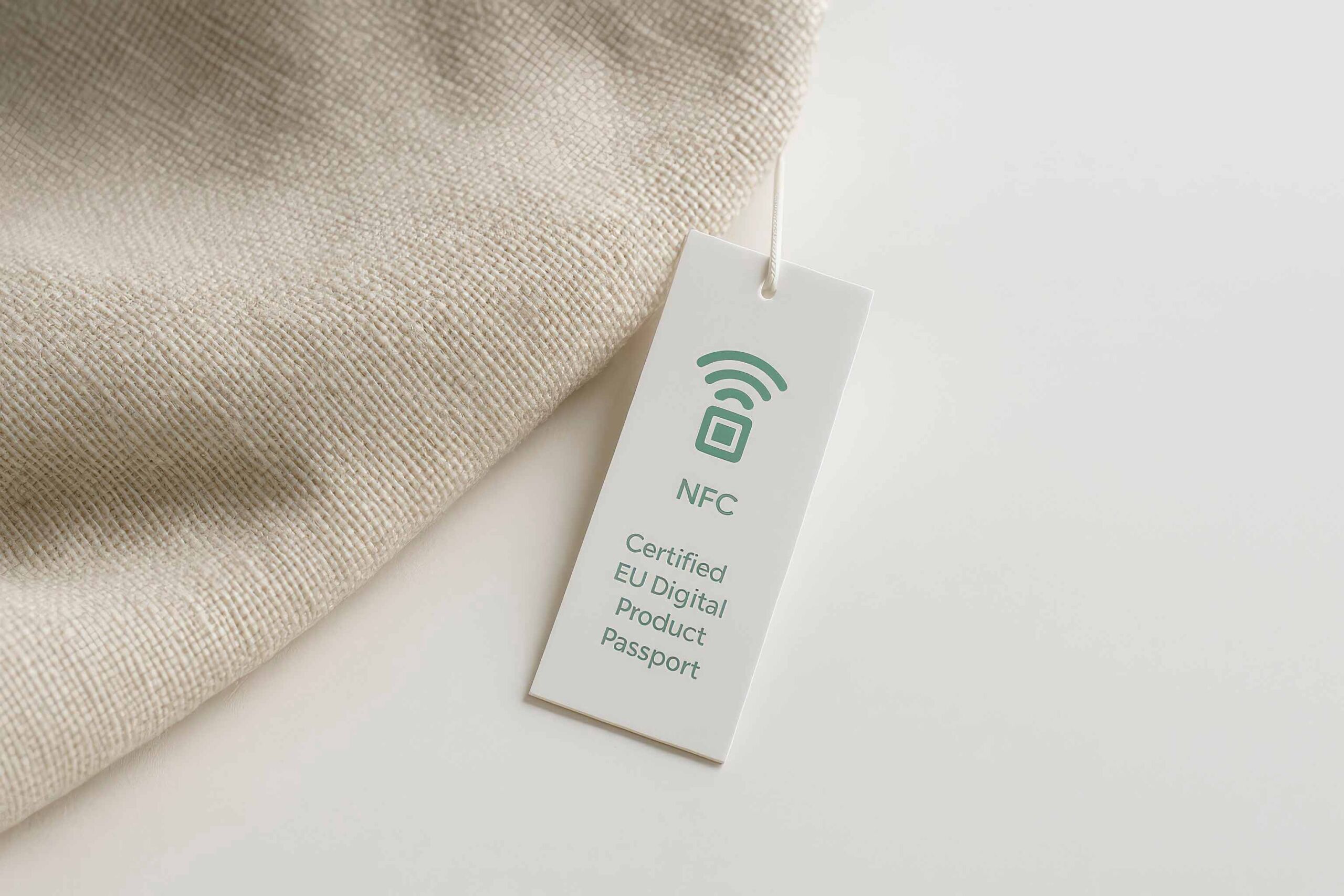 Weißes Hängeetikett für den EU Digital Product Passport mit NFC-Technologie an einem beigen Textilstück