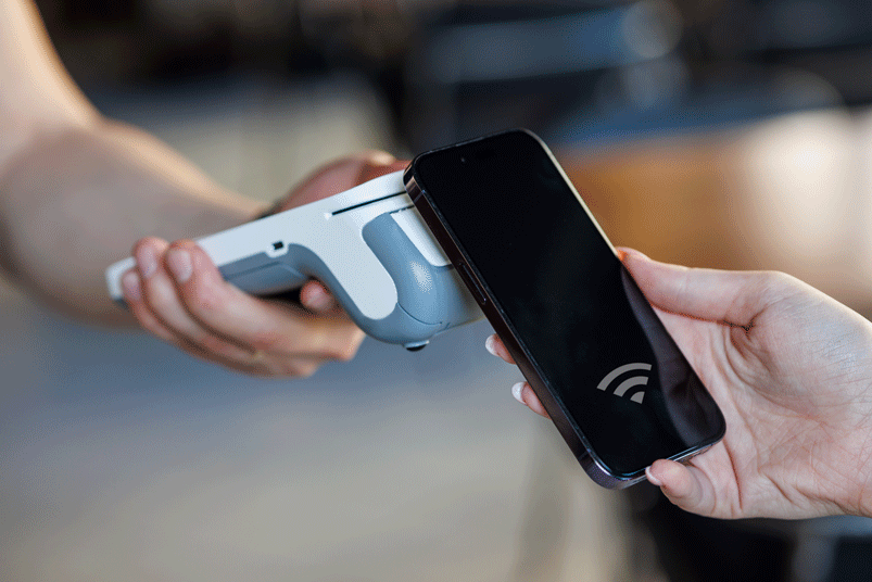NFC-contactless-payments Smartphone, das für eine kontaktlose NFC‑Zahlung an ein Zahlungsterminal gehalten wird.