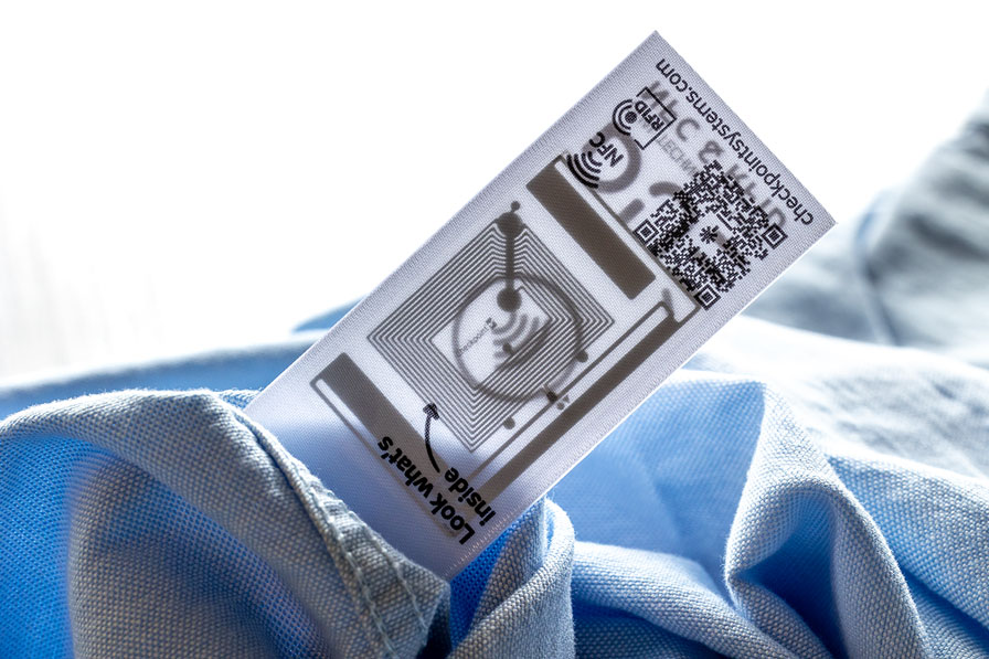 Älykäs RFID-etiketti integroidulla sirulla ja QR-koodilla vaatteessa, kuvastaa älykästä tekstiiliteknologiaa ja muotialan digitalisaatiota.