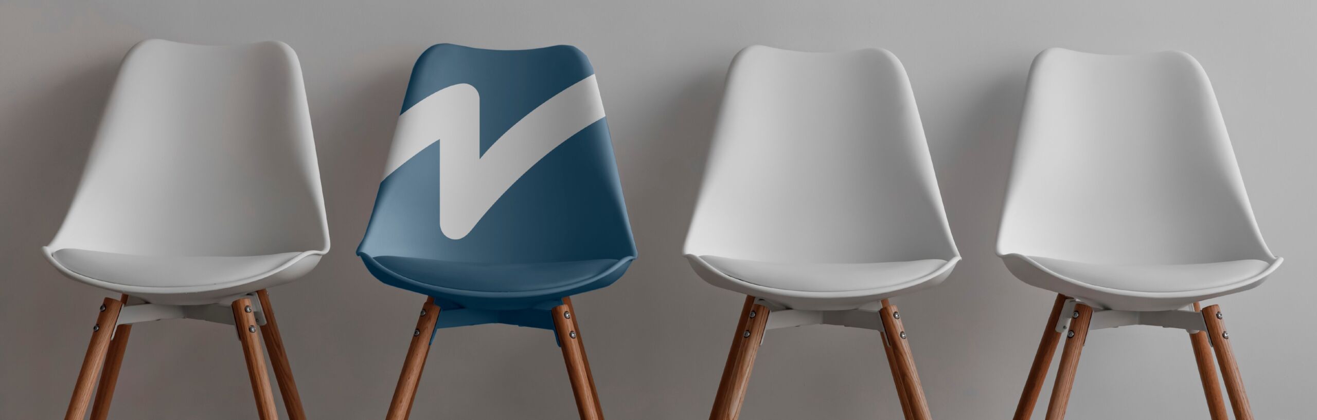 abc58595-24de-4f48-9653-67b369933b16 Vier moderne stoelen op een rij tegen een grijze muur, waarvan drie wit zijn en één blauwe stoel met een groot wit vinkje erop.